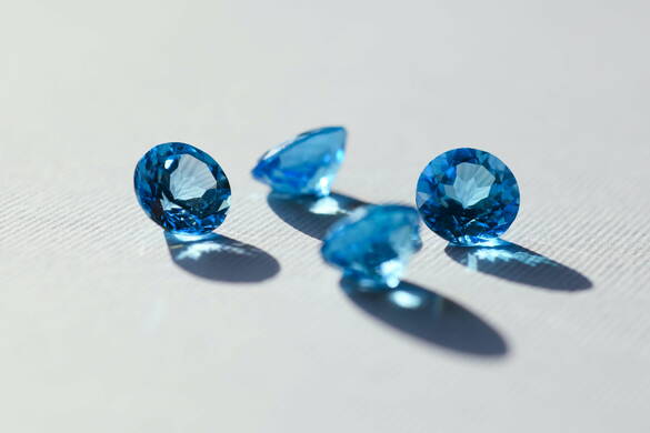 Vier blaue Diamanten auf weissem Hintergrund liegen verstreut auf weissem Untergrund und werfen Schatten.